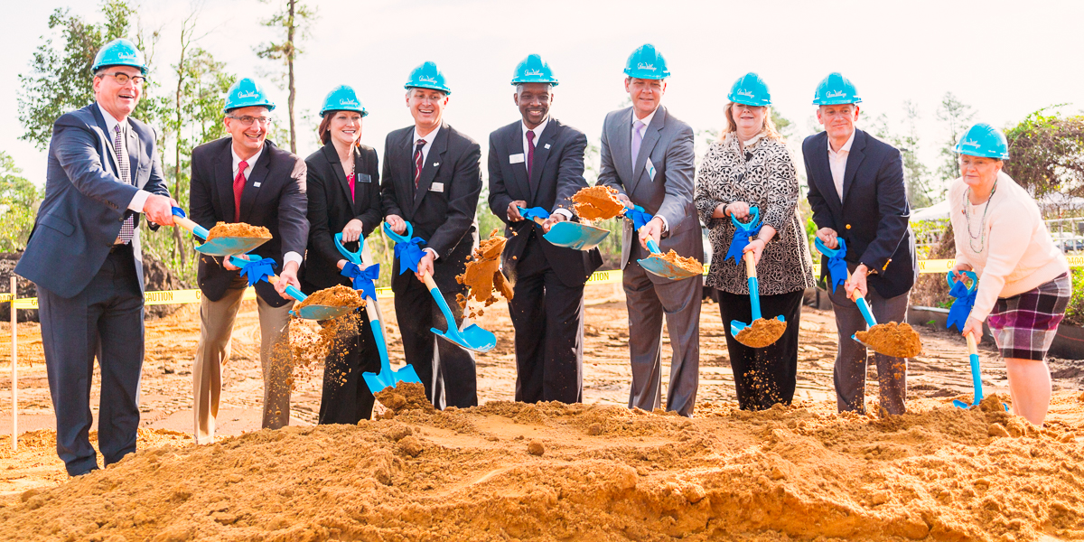 Orlando event videographer shoots a group of nine people in business attire and blue helmets participate in a groundbreaking ceremony, holding shovels as they dig into a pile of dirt.