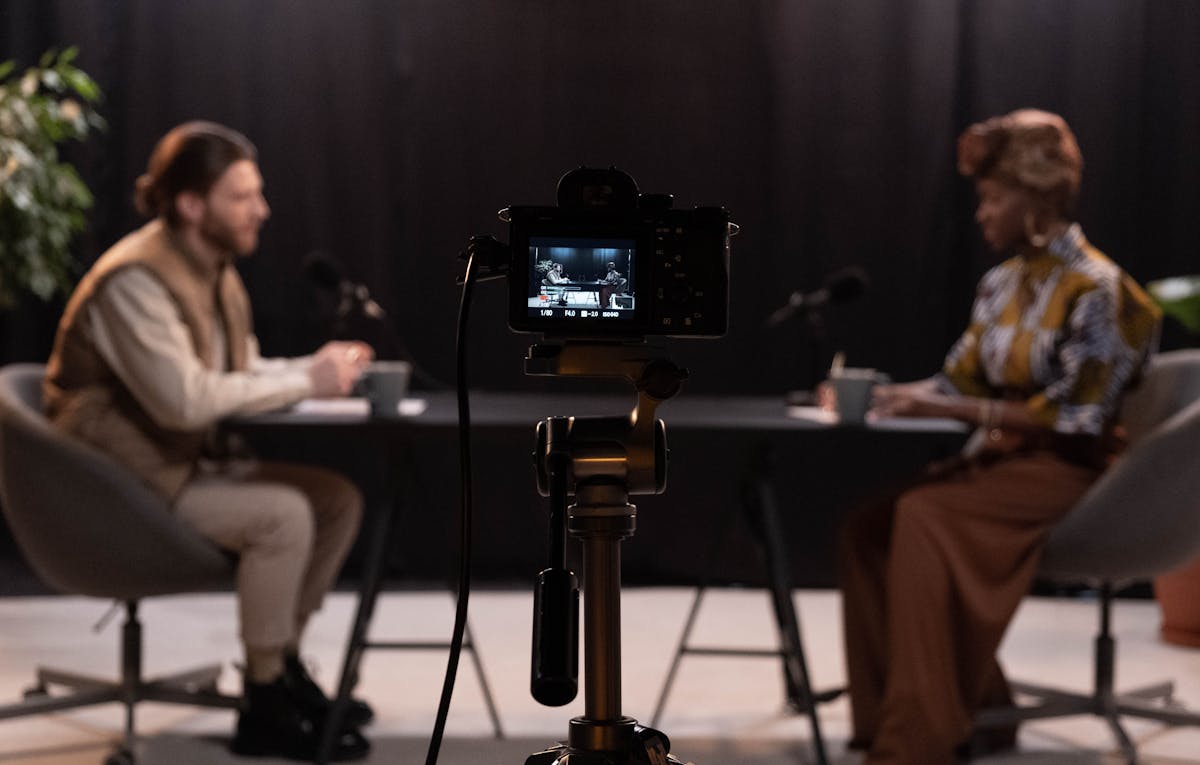 Camera captures two people engaged in a lively podcast interview at a table, exploring intriguing topics like "how much does it cost to make a video?.