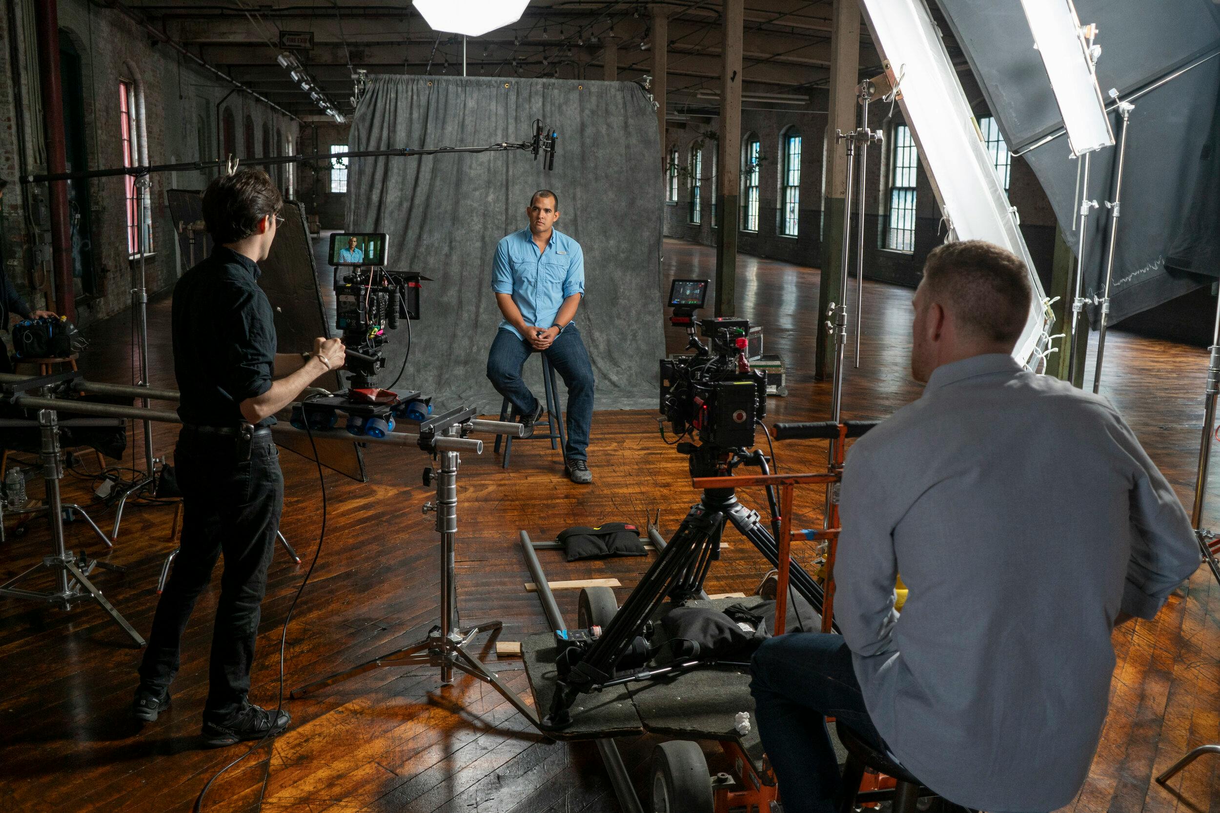 Behind the scenes of a video recording: testimonial video tips with a man in a blue polo sitting on a chair.