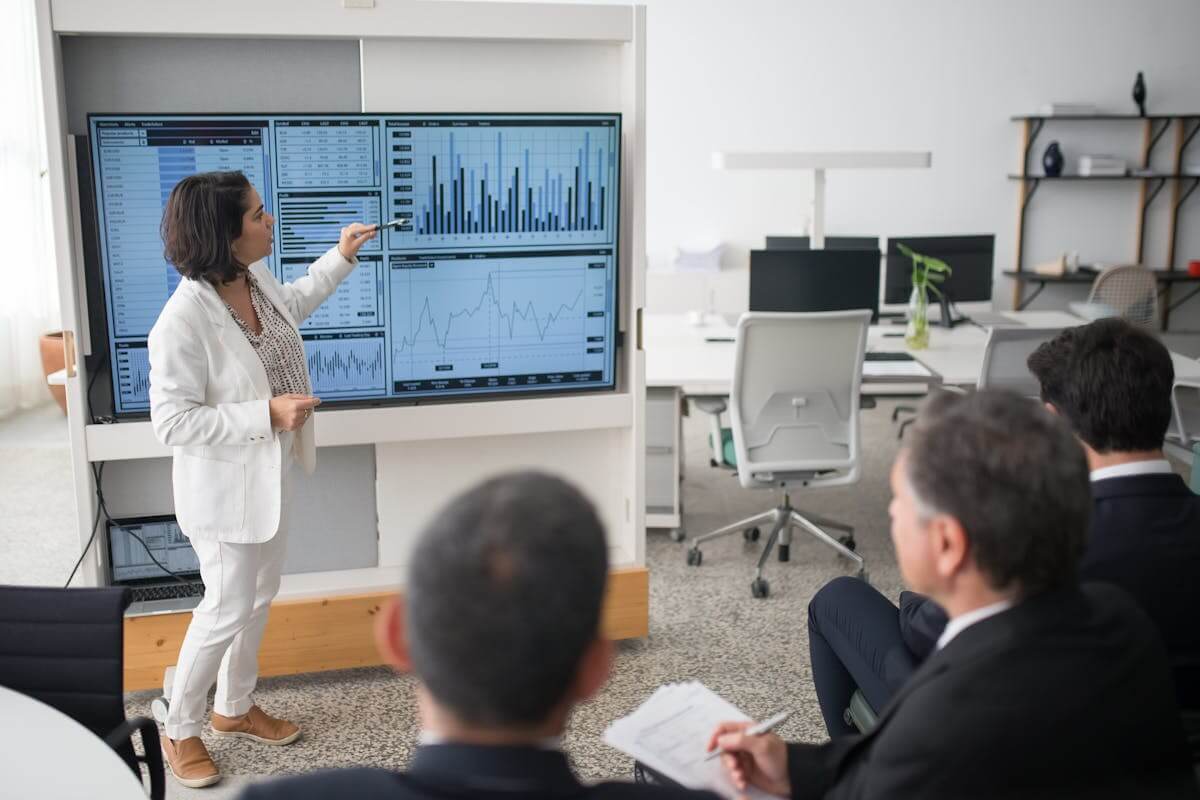 A woman in a white suit presents charts on a screen, showcasing advanced training techniques.