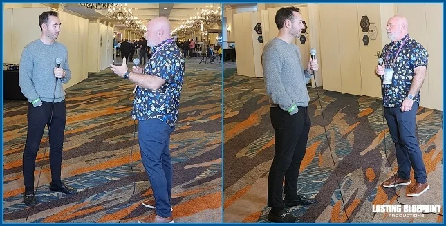 Two men stand talking in a hallway at rosen shingle creek, one holding a microphone, conducting a cybersecurity testimonial interview.